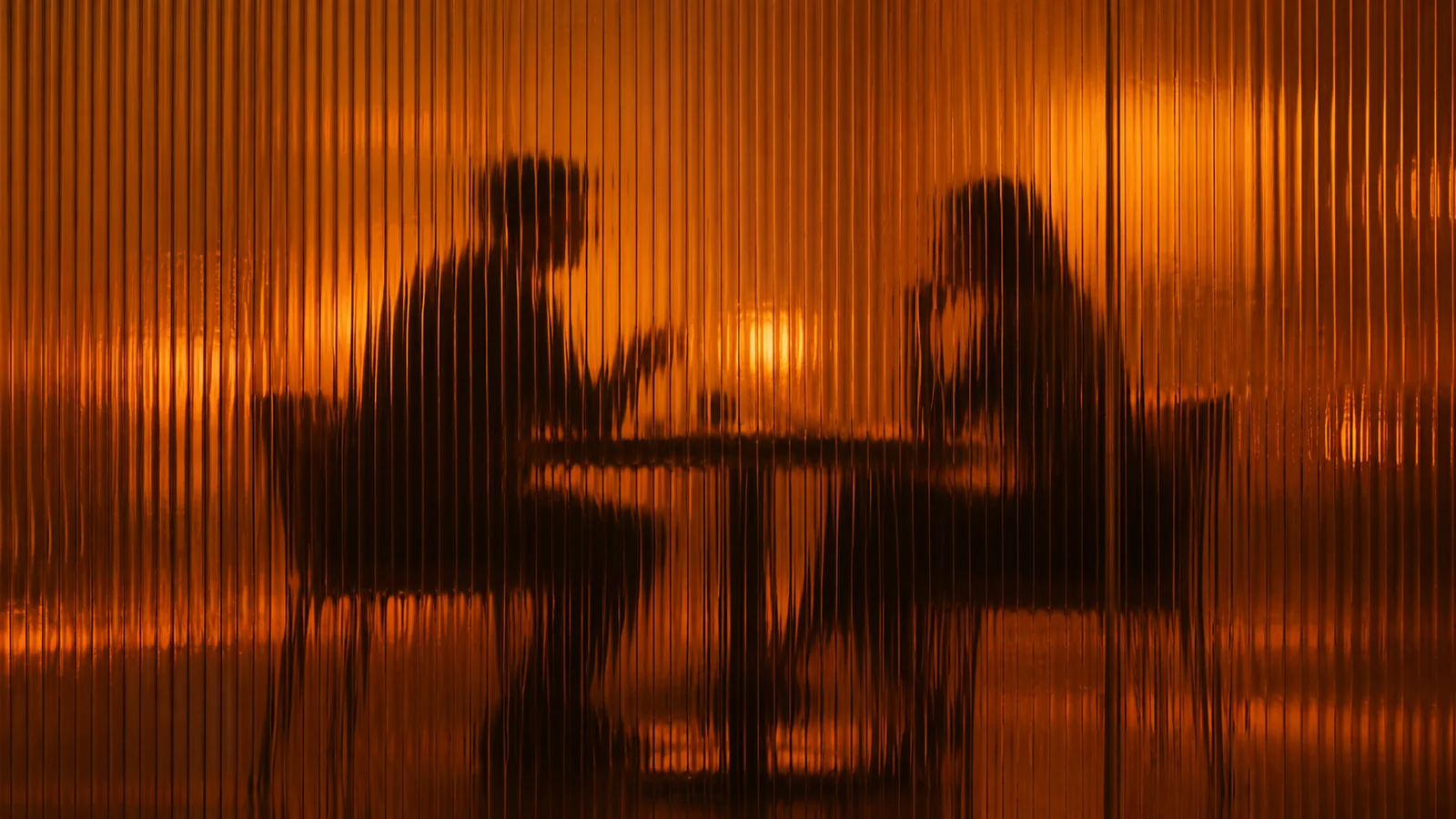 Two people talking across a table behind amber fluted glass.